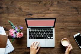 Laptop met roze scherm, koffie, notitieblok en bloemen